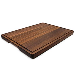 May include: A rectangular wooden cutting board with a dark brown finish. The board has a juice groove around the perimeter and is made of a solid wood with visible grain.