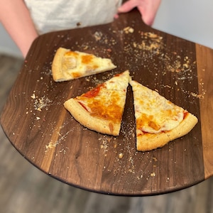 A person is holding a wooden pizza board with three slices of pizza on it.