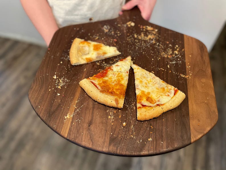 A person is holding a wooden pizza board with three slices of pizza on it.
