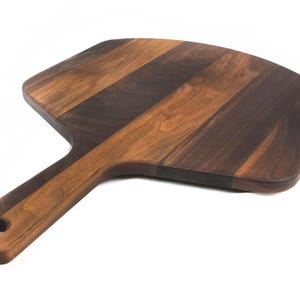 A wooden pizza board with a dark brown finish and a lighter brown handle.