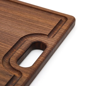 May include: A dark brown wooden cutting board with a built-in handle. The board has a smooth surface and a slightly rounded edge.