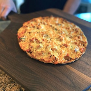 A freshly baked pizza with a golden crust and melted cheese sits on a wooden serving board.