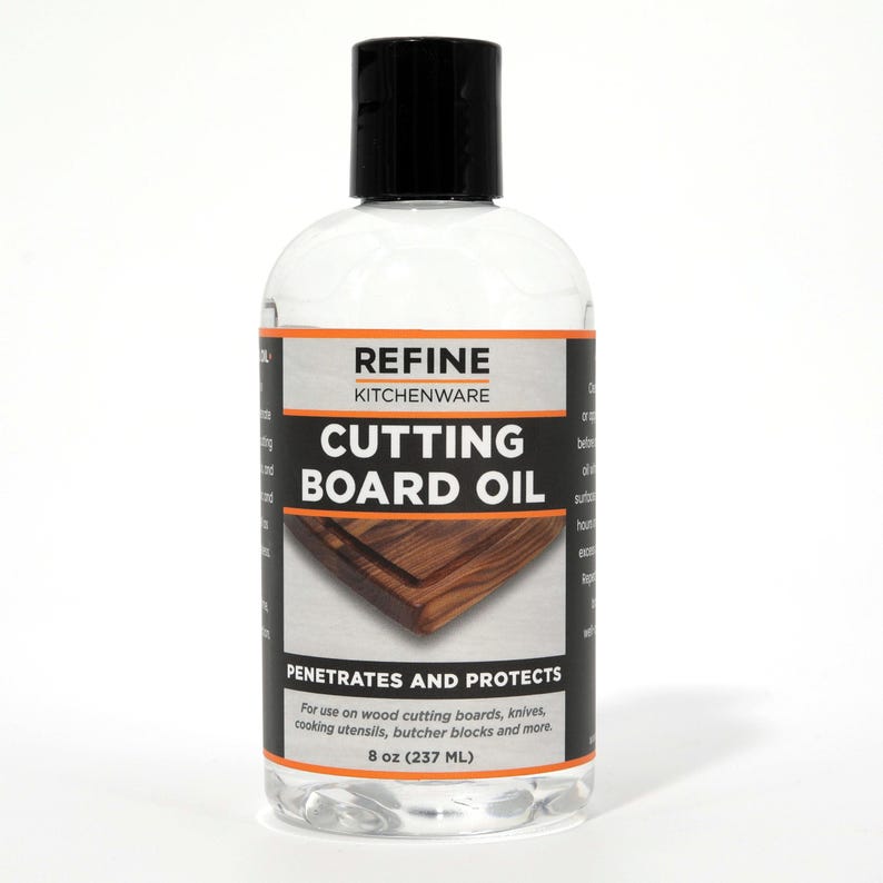 May include: A clear bottle of Refine Kitchenware cutting board oil with a black cap. The label features the text "CUTTING BOARD OIL" and "PENETRATES AND PROTECTS". The bottle contains 237 ml of oil, designed for wood cutting boards and kitchen utensils.