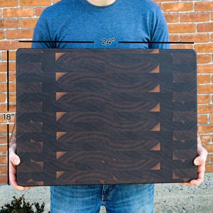A person is holding a large wooden cutting board with a distinctive pattern of dark brown lines.