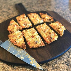 A wooden cutting board holds eight slices of pizza, with a knife resting on it.