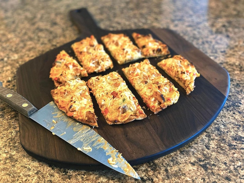 A wooden cutting board holds eight slices of pizza, with a knife resting on it.