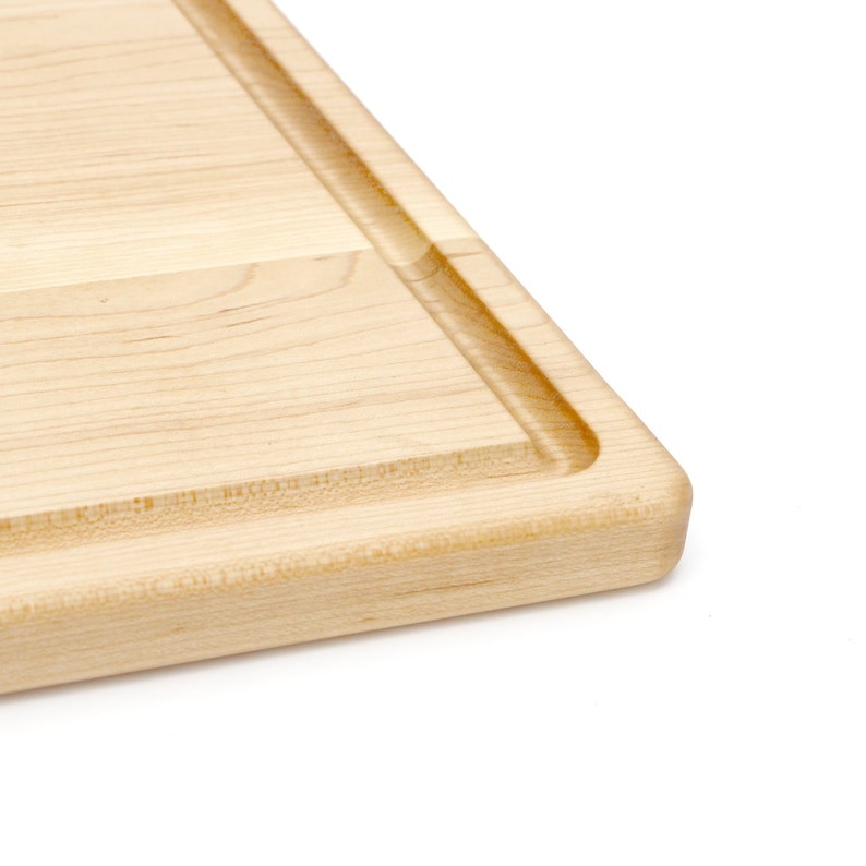 May include: A close-up of the edge of a wooden cutting board. The board is made of light-colored wood and has a raised edge around the perimeter.