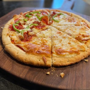 A freshly baked pizza with a golden crust, topped with pepperoni, green peppers, and cheese, sits on a wooden cutting board.