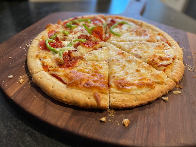 A freshly baked pizza with a golden crust, topped with pepperoni, green peppers, and cheese, sits on a wooden cutting board.