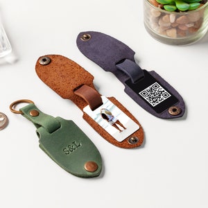 May include: Three leather keychains with different designs. One keychain is green with the initials "S&L" embossed on it. Another keychain is brown with a photo insert and a white background. The third keychain is dark blue with a black QR code.