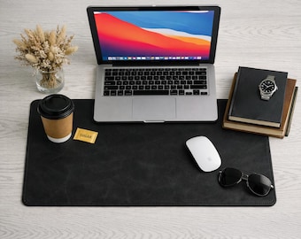 May include: A black leather desk mat with a laptop, coffee cup, and computer mouse. A pair of sunglasses and a watch are on the mat. A small packet of sugar is on the mat. A small bouquet of dried flowers is in a glass vase.