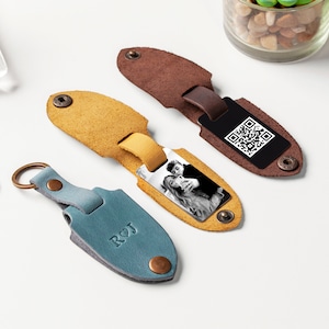 May include: Three leather keychains with different designs. One keychain is blue with the initials "RCJ" and a heart. Another keychain is yellow with a photo of a couple. The third keychain is brown with a black QR code.