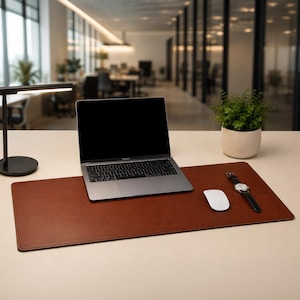May include: A brown leather desk mat with a laptop, mouse, and watch. A black desk lamp and a small potted plant are also on the desk. The laptop is open, displaying a black screen. The watch has a black leather band.