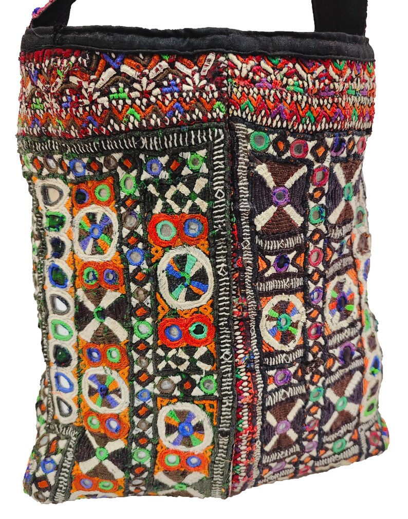 K&ouml;nnte beinhalten: Eine farbenfrohe, bestickte Umh&auml;ngetasche mit schwarzem Riemen. Die Tasche zeigt komplizierte Muster in Rot, Orange, Gr&uuml;n, Blau und Wei&szlig;, mit kleinen Spiegelakzenten. Das Design ist eine Mischung aus geometrischen Formen und floralen Motiven.