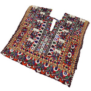 Puede incluir: Un panel de tela bordada de colores con intrincados patrones geométricos y adornos de espejo. La tela es principalmente marrón con acentos de rojo, verde, azul y amarillo.