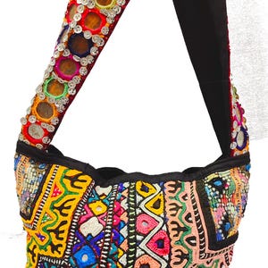 Puede incluir: Un bolso de hombro de patchwork colorido con detalles bordados y acentos de espejo circulares. El bolso tiene una correa negra con un diseño similar.