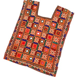 Puede incluir: Textil bordado naranja con escote cuadrado. La tela presenta un patrón geométrico de cuadrados en naranja, rojo, azul y verde, con pequeños acentos de espejo. Los bordes están adornados con un borde detallado y multicolor.