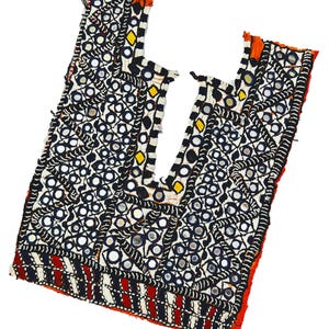 May include: A vintage textile top with detailed mirror and beadwork. The top has a geometric pattern in black, white, and red, with yellow and orange accents. The design incorporates small, round mirrors and is likely handmade.