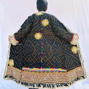 May include: A black coat with a geometric pattern of yellow dots and lines. The coat has a faux fur trim and colourful embroidered details along the hem and sleeves. The coat is open, revealing the lining.