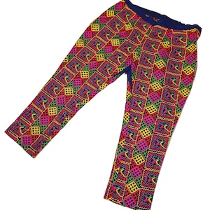 May include: Brightly coloured patterned trousers with a geometric design in pink, yellow, green, and blue. The trousers have a dark blue waistband and a repeating square pattern. The fabric appears to be lightweight.