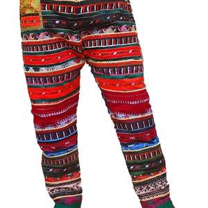 May include: Vibrant patterned trousers with a drawstring waist and pockets. The design features a mix of red, green, black, and blue horizontal stripes and geometric patterns. The fabric looks lightweight, suitable for casual wear. The waist is elasticated.