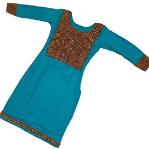 May include: A teal-colored tunic dress with long sleeves. The bodice features a brown embroidered panel with small mirrored accents. The cuffs and hemline are also adorned with similar embroidery. The dress has a round neckline and a relaxed fit.