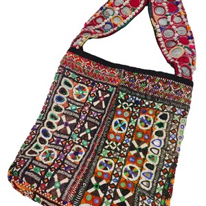 K&ouml;nnte beinhalten: Eine farbenfrohe, bestickte Umh&auml;ngetasche mit rechteckiger Form. Die Tasche weist komplizierte Muster in verschiedenen Farben auf, darunter Rot, Blau, Gr&uuml;n und Orange. Der Tr&auml;ger ist mit reflektierenden, kreisf&ouml;rmigen Verzierungen versehen.