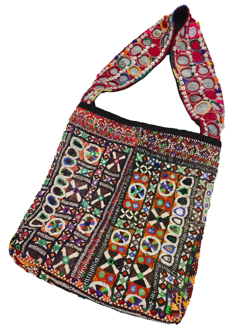 K&ouml;nnte beinhalten: Eine farbenfrohe, bestickte Umh&auml;ngetasche mit rechteckiger Form. Die Tasche weist komplizierte Muster in verschiedenen Farben auf, darunter Rot, Blau, Gr&uuml;n und Orange. Der Tr&auml;ger ist mit reflektierenden, kreisf&ouml;rmigen Verzierungen versehen.