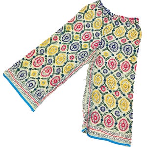 May include: Wide-leg pants featuring an off-white base with an intricate, repeating geometric pattern embroidered in vibrant yellow, hot pink, and dark blue thread. The garment includes a blue hemline and a gathered elastic waistband at the top.