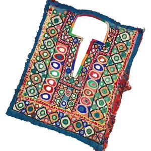 Puede incluir: Textil bordado colorido, de forma cuadrada, con abertura para el cuello. El textil presenta una vibrante gama de colores, incluyendo rojo, azul, verde y amarillo, con intrincados patrones geométricos y detalles de espejo. Los bordes están ribeteados con tela azul oscuro.