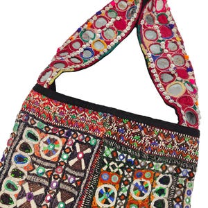 K&ouml;nnte beinhalten: Bunte, bestickte Umh&auml;ngetasche mit schwarzem Riemen. Die Tasche weist komplizierte Muster in verschiedenen Farben auf, darunter Rot, Orange, Gr&uuml;n und Blau, mit kleinen Spiegeln im Design. Der Riemen der Tasche ist ebenfalls mit Spiegeln verziert.