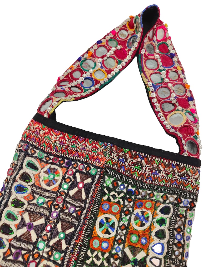 K&ouml;nnte beinhalten: Bunte, bestickte Umh&auml;ngetasche mit schwarzem Riemen. Die Tasche weist komplizierte Muster in verschiedenen Farben auf, darunter Rot, Orange, Gr&uuml;n und Blau, mit kleinen Spiegeln im Design. Der Riemen der Tasche ist ebenfalls mit Spiegeln verziert.