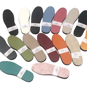 May include: Assortment of 15 leather shoe soles in various colors, including black, white, green, brown, orange, red, blue, and gray. The soles are all the same size and shape, and they have a textured surface.