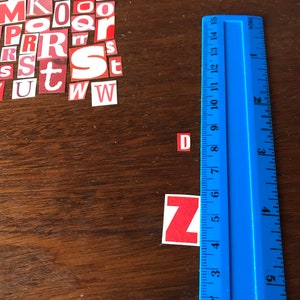 Puede incluir: Azulejos de letras rojas y blancas que deletrean la palabra "DZ" sobre una superficie de madera con una regla azul.