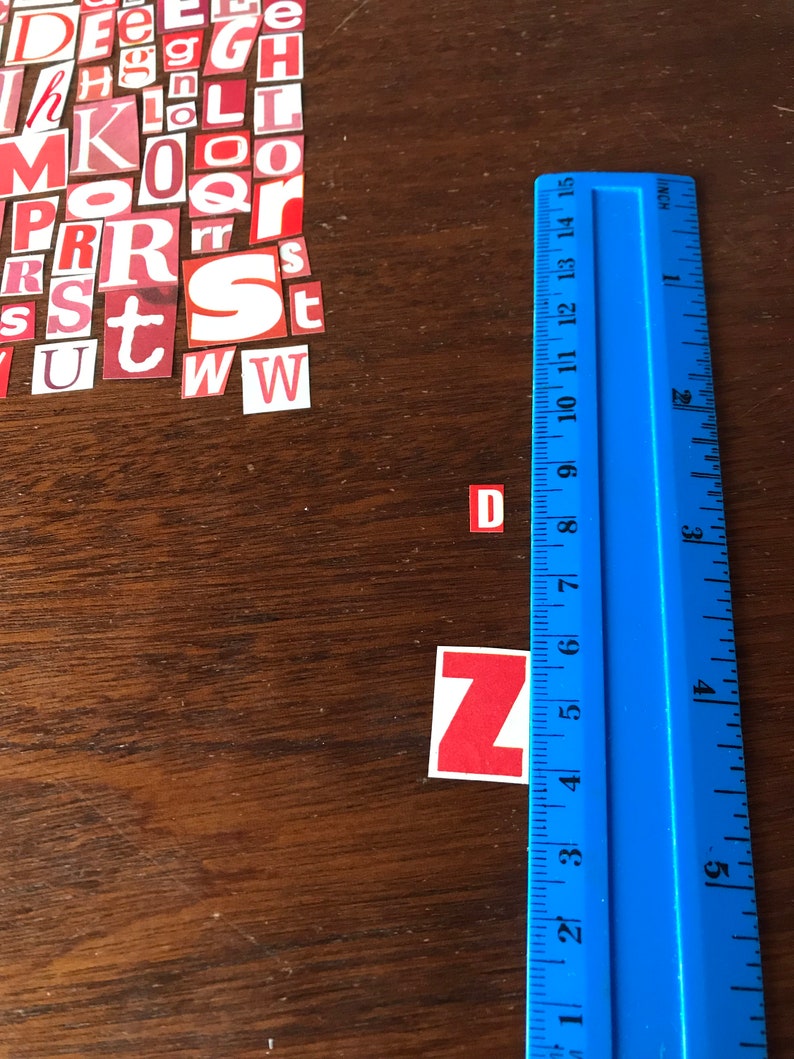 Puede incluir: Azulejos de letras rojas y blancas que deletrean la palabra "DZ" sobre una superficie de madera con una regla azul.