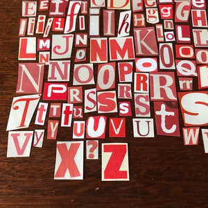 Puede incluir: Una colecci&oacute;n de letras del alfabeto de papel rojo y blanco, recortadas de revistas o peri&oacute;dicos, dispuestas sobre una superficie de madera marr&oacute;n.