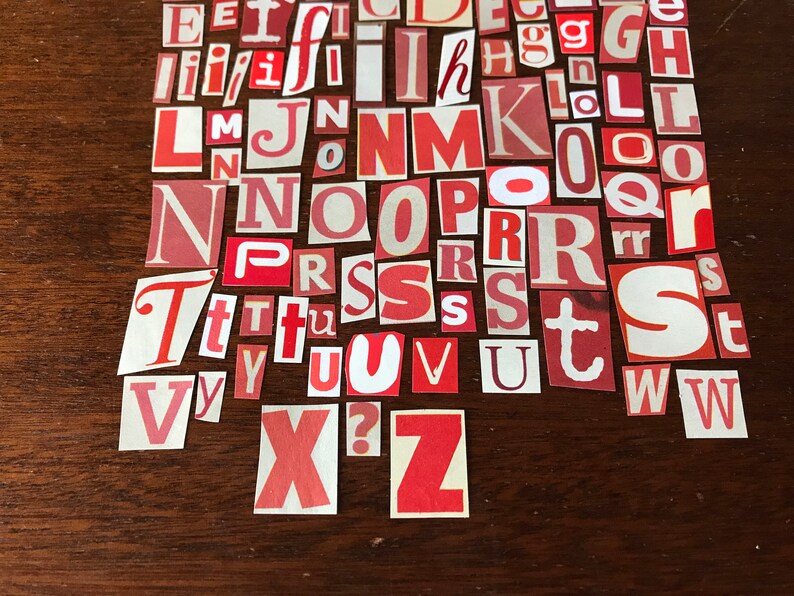 Puede incluir: Una colecci&oacute;n de letras del alfabeto de papel rojo y blanco, recortadas de revistas o peri&oacute;dicos, dispuestas sobre una superficie de madera marr&oacute;n.
