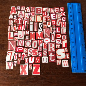 Puede incluir: Una colecci&oacute;n de letras del alfabeto de papel rojo y blanco, recortadas de revistas o peri&oacute;dicos, dispuestas en un patr&oacute;n aleatorio sobre una superficie de madera marr&oacute;n. Las letras son ligeramente desiguales y algunas est&aacute;n ligeramente curvadas.