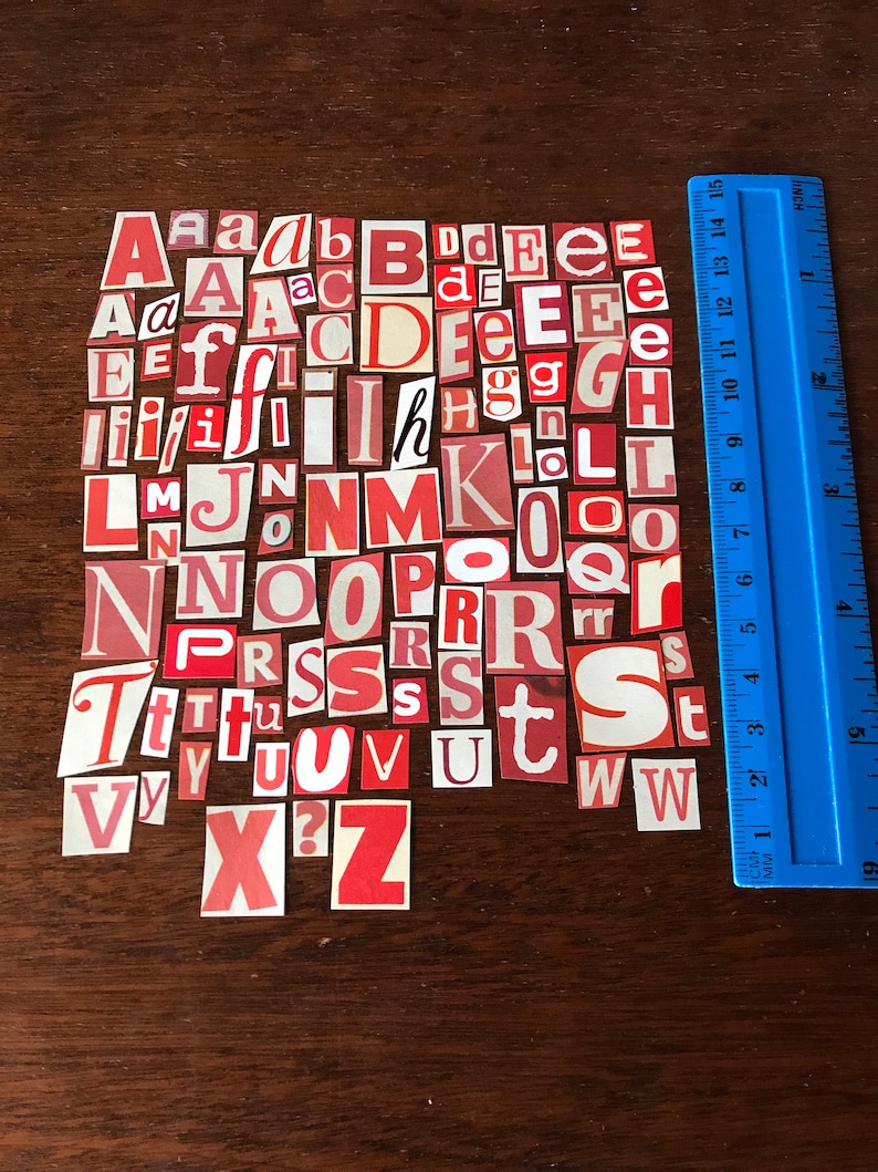 Puede incluir: Una colecci&oacute;n de letras del alfabeto de papel rojo y blanco, recortadas de revistas o peri&oacute;dicos, dispuestas en un patr&oacute;n aleatorio sobre una superficie de madera marr&oacute;n. Las letras son ligeramente desiguales y algunas est&aacute;n ligeramente curvadas.