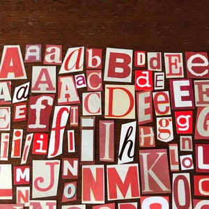 Puede incluir: Una colecci&oacute;n de letras rojas, blancas y crema cortadas de papel y dispuestas en un patr&oacute;n aleatorio sobre una superficie de madera marr&oacute;n. Las letras incluyen A, B, C, D, E, F, G, H, I, J, K, L, M, N, O.
