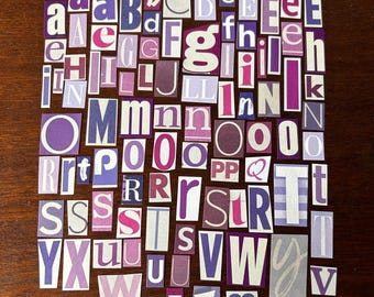 Puede incluir: Una colección de letras recortadas de varios tamaños y fuentes, dispuestas sobre una superficie de madera oscura. Las letras son principalmente en tonos de morado, rosa y blanco, creando un efecto de collage. Las letras son de revistas y periódicos.