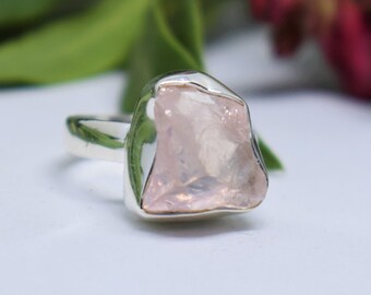 May include: A silver ring with a large, raw, pink quartz stone. The stone is irregularly shaped and has a natural, rough texture.
