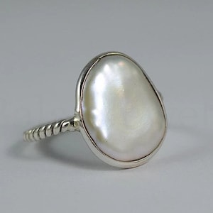 Peut inclure: Une bague en argent avec une perle baroque blanche sertie dans un sertissage à bélière. La bande est torsadée et a une texture de corde.