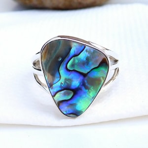 May include: A silver ring featuring a triangular abalone shell inlay. The shell displays iridescent blue, green, and brown hues.