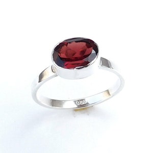 May include: A silver ring with a red oval gemstone. The ring is marked with "925" on the inside band.