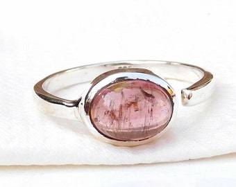 May include: A silver ring with a pink oval gemstone. The ring is open on one side and has a smooth, polished finish.