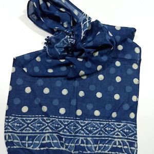 May include: A blue cotton scarf with white polka dots and a white border design. The scarf has a fringe trim with blue pom-poms.