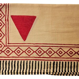 May include: A beige textile with a large red triangle and a border of red diamonds and black vertical stripes. The fabric is folded, showing the pattern on the top layer.