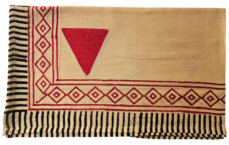 May include: A beige textile with a large red triangle and a border of red diamonds and black vertical stripes. The fabric is folded, showing the pattern on the top layer.