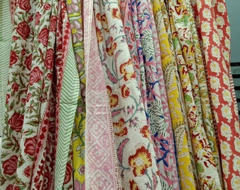 May include: A collection of colorful cotton scarves with floral patterns. The scarves are hanging on a rack and are arranged in a variety of colors, including pink, yellow, green, and red.